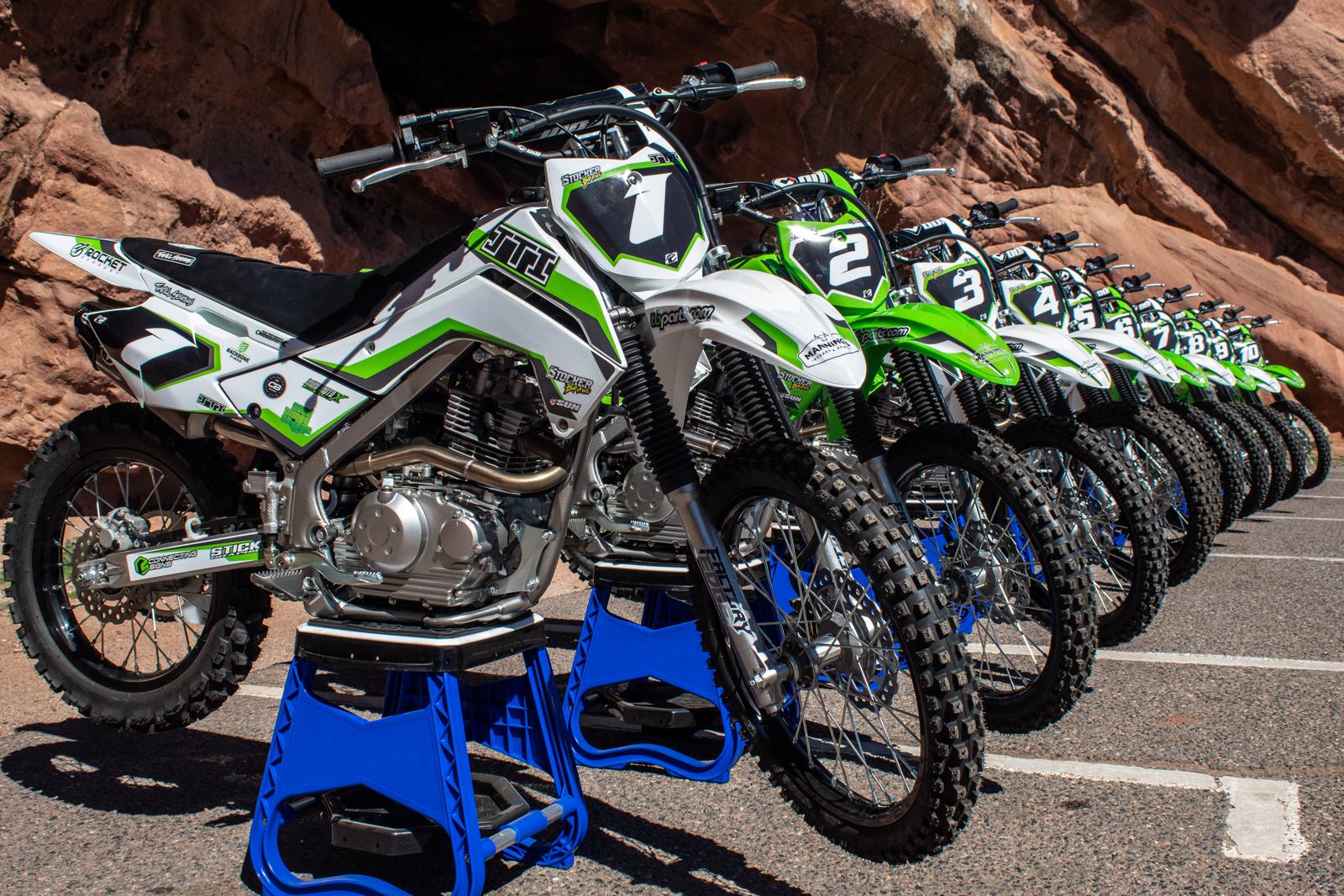 Fleet of Kawasaki KLX140RL race bikes lined up, numbered 1 through 10